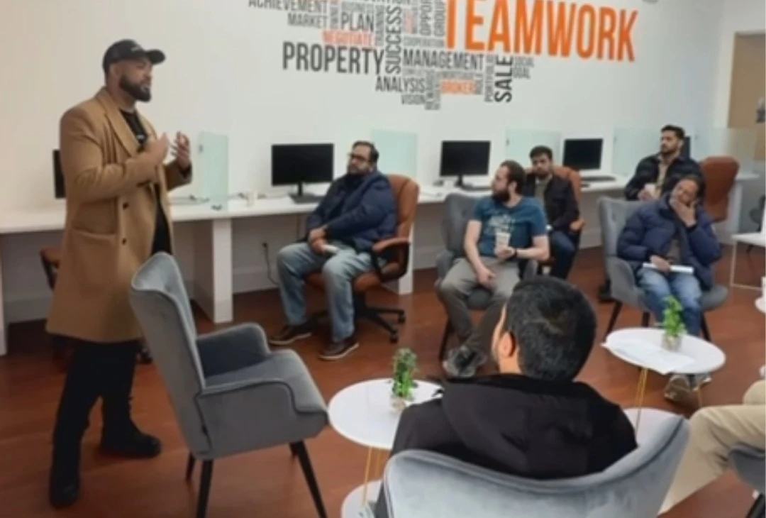 A presenter addressing seated attendees in an Amin Realty meeting room.