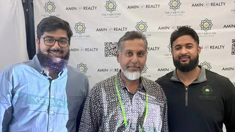 Three adults in front of a Fajr Fund and Amin Realty booth backdrop.