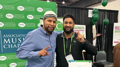 Two adults, one wearing a Fajr polo, together at an ISNA booth.